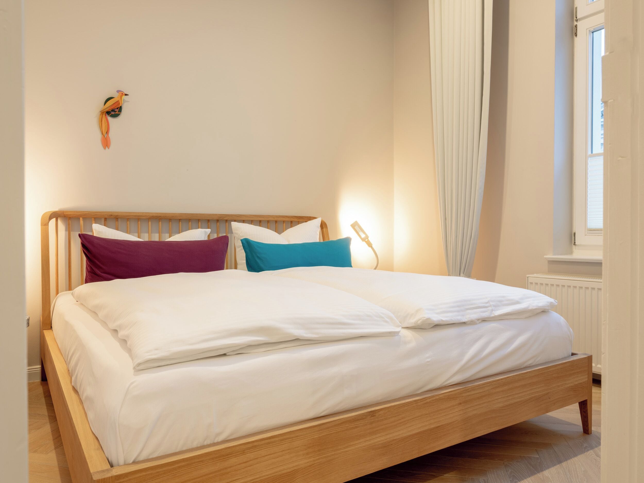 Ein ordentlich bezogenes Bett mit weißen Leinen, einem hölzernen Kopfteil und einer kleinen Vogeldekoration an der Wand.