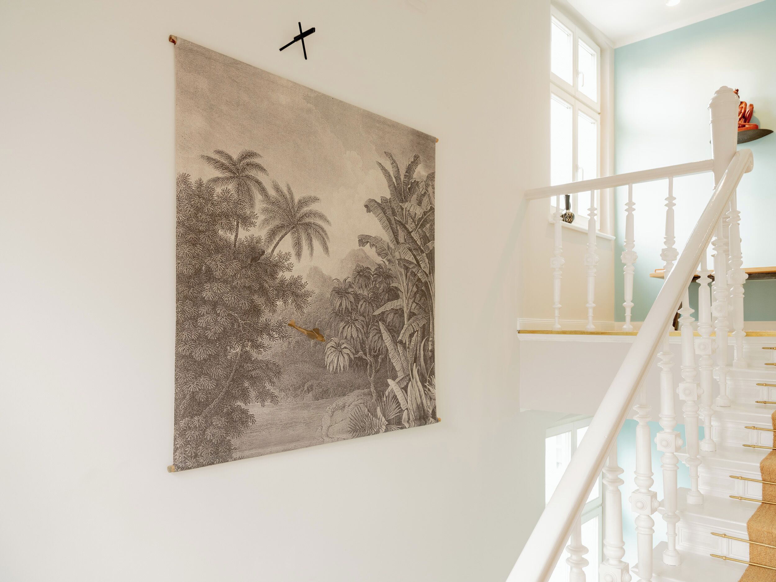 A staircase with white balusters and a handrail, leading to a landing with a large framed botanical illustration on the wall.