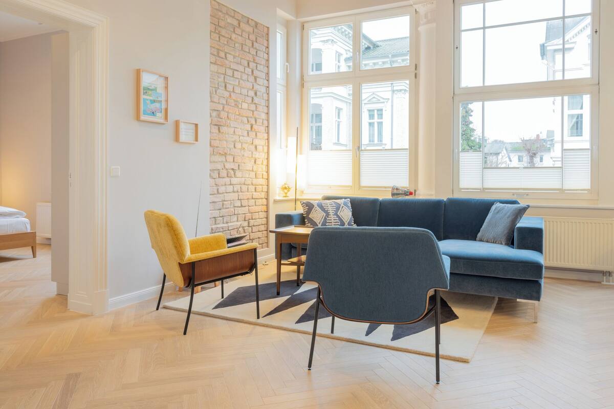 Una sala de estar moderna con una pared de ladrillo decorativa, un sofá azul, un sillón amarillo y una mesa de centro de madera.