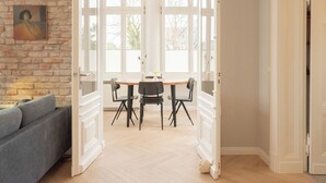 Un espace de vie et de salle à manger à aire ouverte, avec un mur en briques, un canapé gris, une table à manger en bois et quatre chaises, ainsi que de grandes fenêtres.