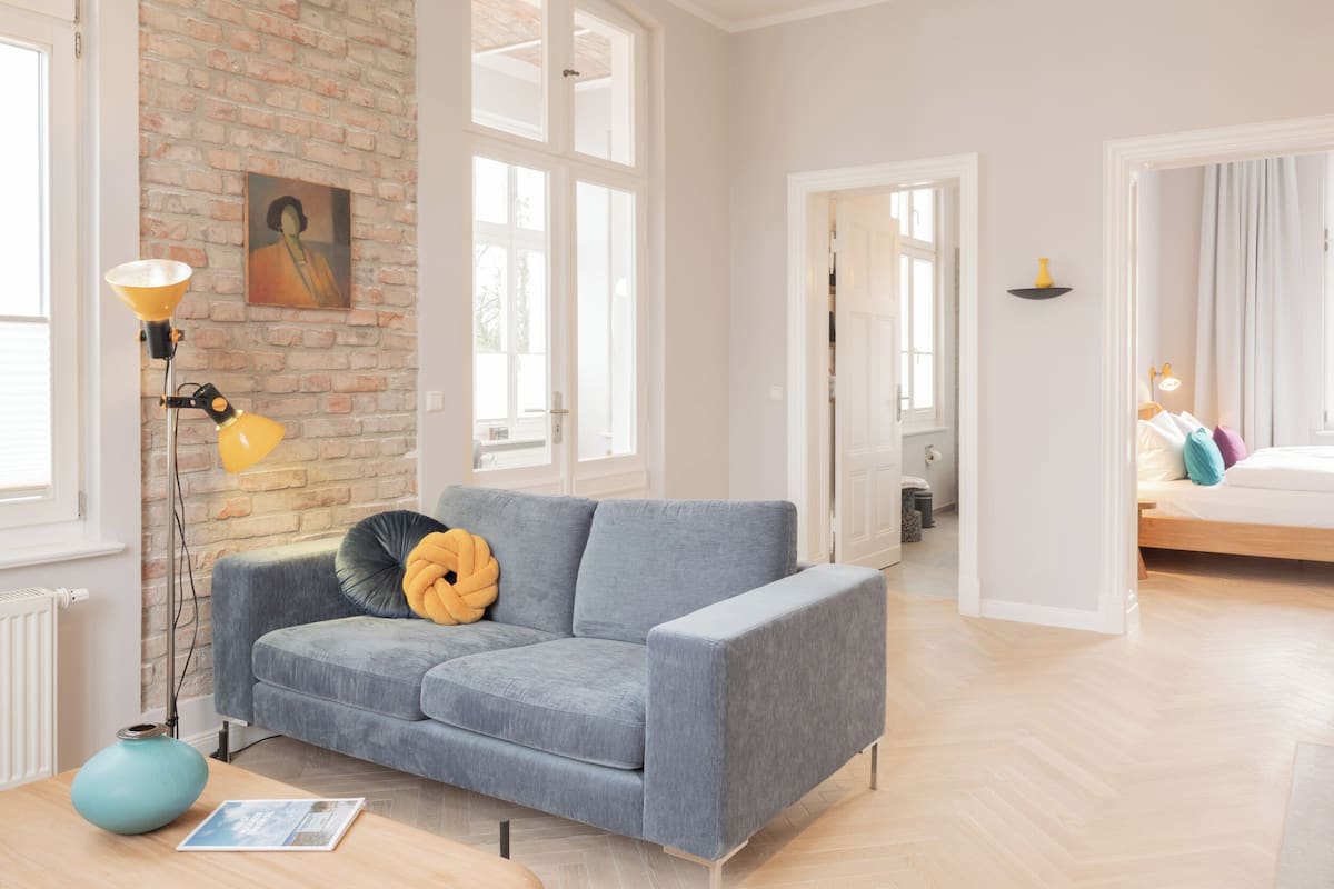 Una sala moderna con un sofá gris, una lámpara de pie y un florero azul sobre una mesa de madera.