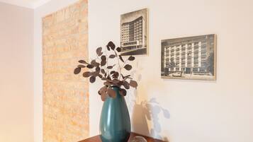 A room with a brick wall, a blue vase with dried leaves, and two framed pictures on the wall.