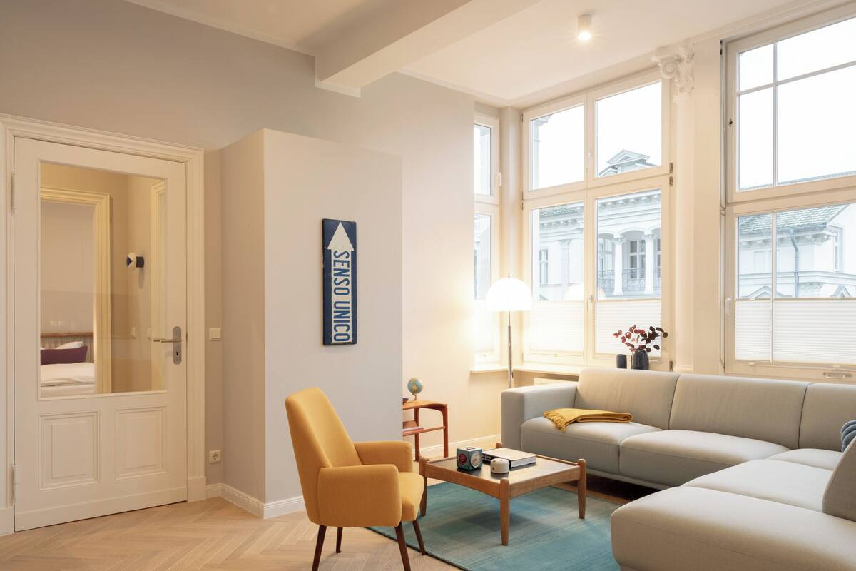 Una sala de estar moderna con sofá, sillón, mesa de centro y un ventanal con vistas a edificios.