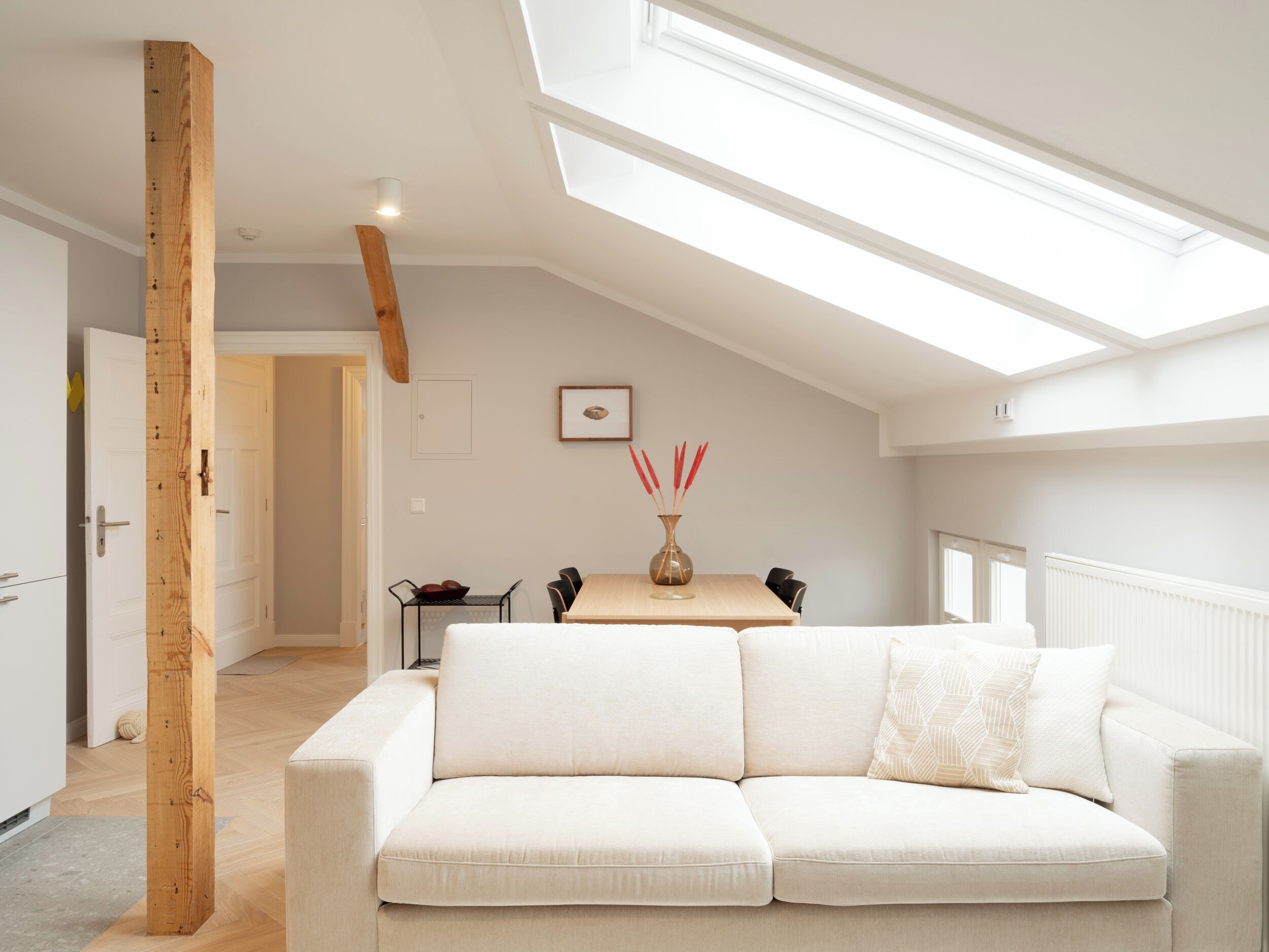 A modern loft-style room with a sloped ceiling, a white sofa, a dining table with chairs, and a skylight.