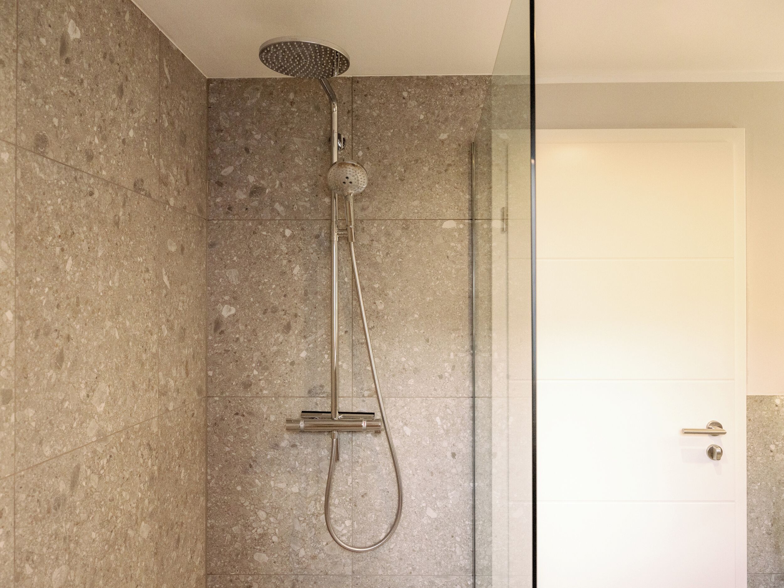Een moderne douche met een handdouche en een vastgelegde douchekop, gemonteerd op een wand met spikkelende tegels.