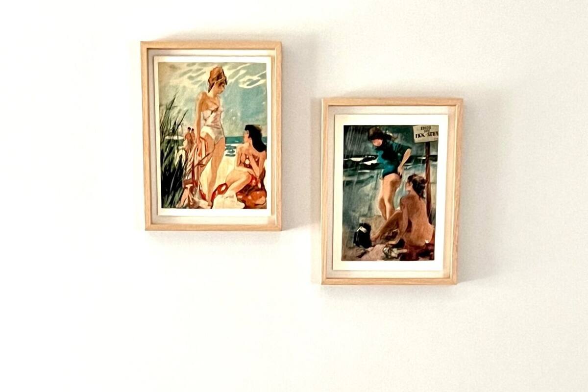 Dos cuadros enmarcados en una pared, un taburete pequeño al frente.