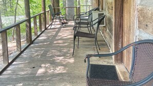A wooden porch with a covered seating area, including metal chairs and a bench. - Cabins In The Pines Unit 2-Covered Porch -  - Charcoal Grill - Wood Fireplace (Cherokee)