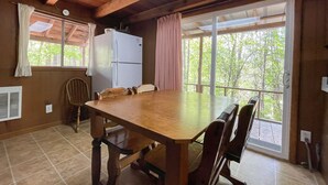 A wooden dining table with chairs, a refrigerator, and a window with curtains. - Cabins In The Pines Unit 2-Covered Porch -  - Charcoal Grill - Wood Fireplace (Cherokee)