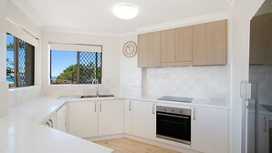 A modern kitchen with white cabinetry, a built-in oven, and a window with a view of the outdoors. - Point View Lodge 2 - Ground Floor Beachfront Bilinga - Linen Provided (Bilinga)