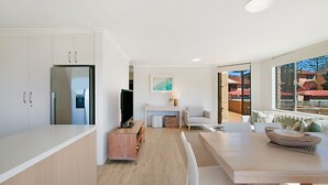 A modern kitchen with white cabinetry, a built-in refrigerator, and a dining area with a wooden table and chairs. - Point View Lodge 2 - Ground Floor Beachfront Bilinga - Linen Provided (Bilinga)