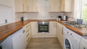 A compact kitchen with a built-in oven, a washing machine, and a coffee maker. - Waters Reach (Kingsbridge)