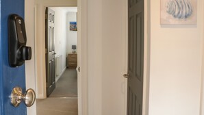 En hall med en blå dörr till vänster, en vit dörr till höger och en tavla på väggen.