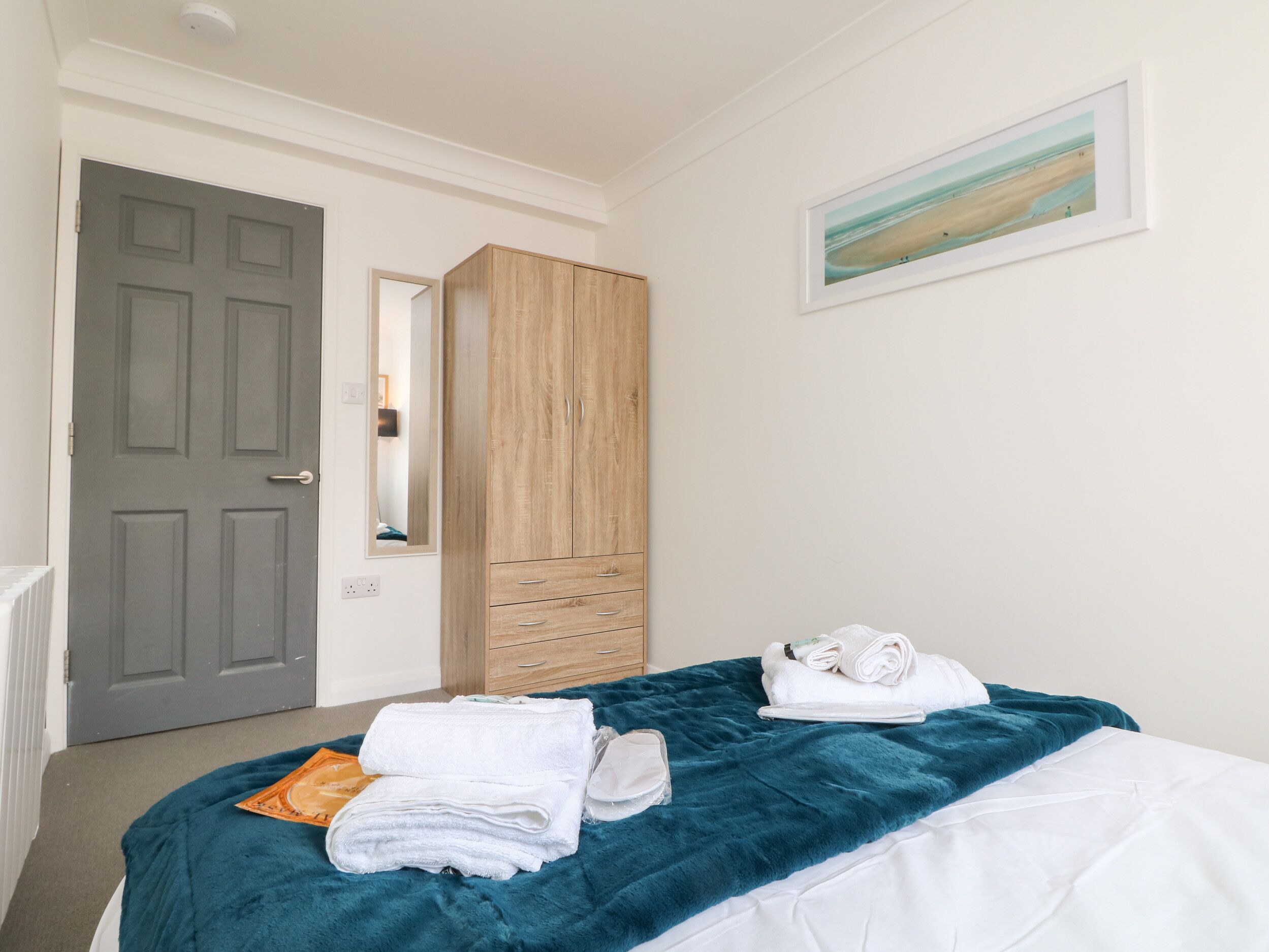 Ein Schlafzimmer mit einem Bett, einem Holzschrank, einem Spiegel und einem gerahmten Bild an der Wand.