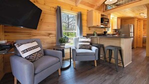 Een gezellig cabinteertier met een bank, fauteuil en barstoelen, houten vloeren en een keukenhoek.