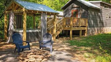 Une cabane dotée d’une terrasse en bois, d’un foyer en pierre et de deux fauteuils Adirondack.