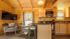 Een houten chalet van binnen met een televisie, keuken, eethoek en bar.