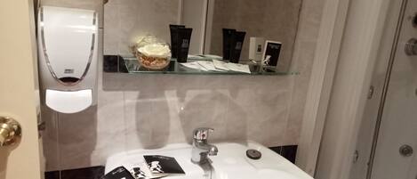 A bathroom with a white sink, a hand dryer, and toiletries on a shelf.
