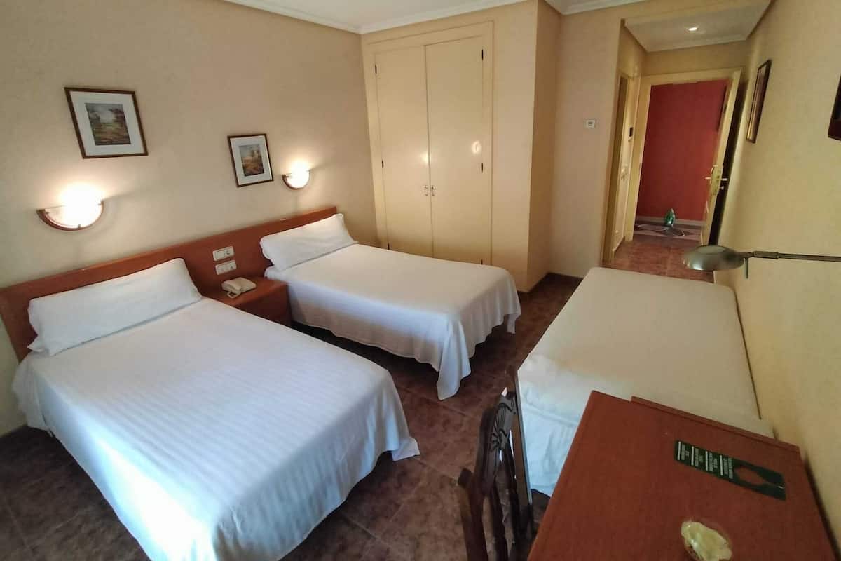 Une chambre d’hôtel avec deux lits simples, un bureau, une chaise, une petite table, un téléphone et une porte donnant sur une autre chambre.