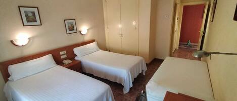 Habitación de hotel con dos camas individuales, un escritorio, una silla, una mesita y un teléfono, con puerta que da a otra habitación.