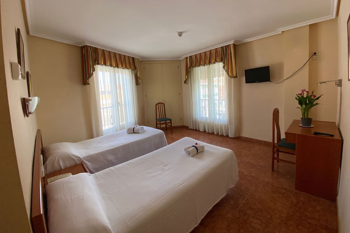 Une chambre d’hôtel avec deux lits, un bureau, une chaise, une télévision et une fenêtre avec des rideaux.