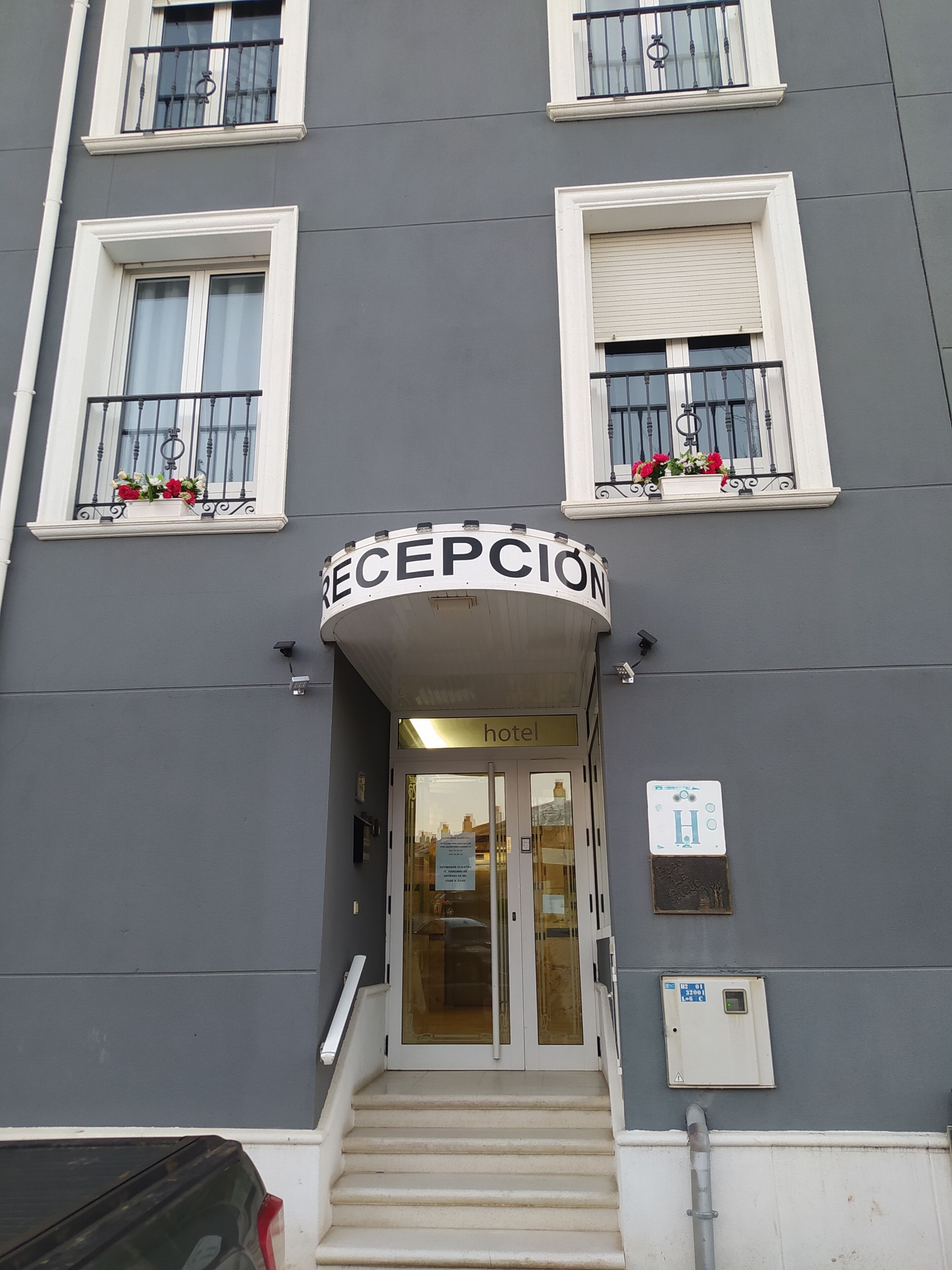 A hotel entrance with a reception sign, double doors, and a staircase leading up.