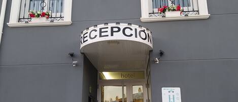 Entrada de hotel con un cartel de recepción, puertas dobles y una escalera que sube.