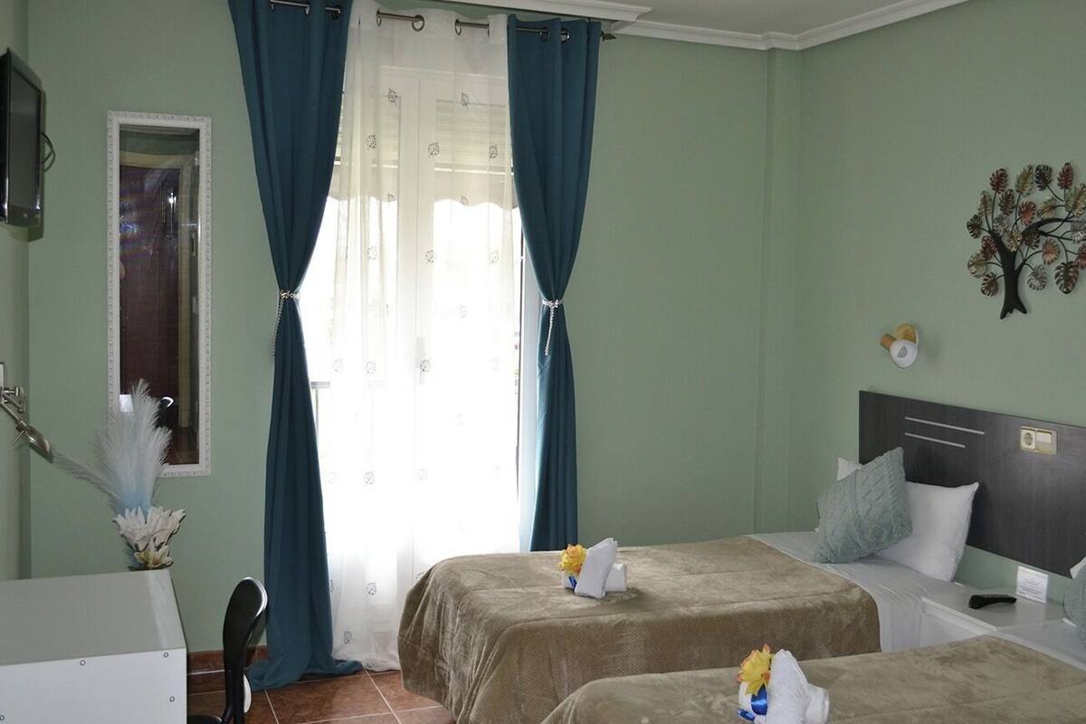 Une chambre d’hôtel avec deux lits, un bureau, une chaise, un miroir et une fenêtre avec des rideaux.