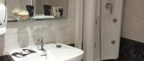 Un baño con lavamanos blanco, ducha y espejo sobre el lavamanos.