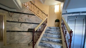 A marble staircase with a wooden handrail and metal balusters, leading to an elevator. - El pozo de la Nieve (Tordesillas)