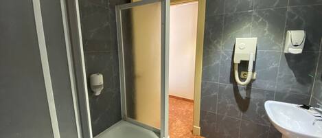 A bathroom with a glass shower enclosure, a sink, and two hand sanitizer dispensers on the wall.