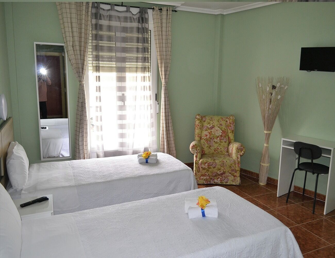 A hotel room with two beds, a chair, a desk, and a mirror.