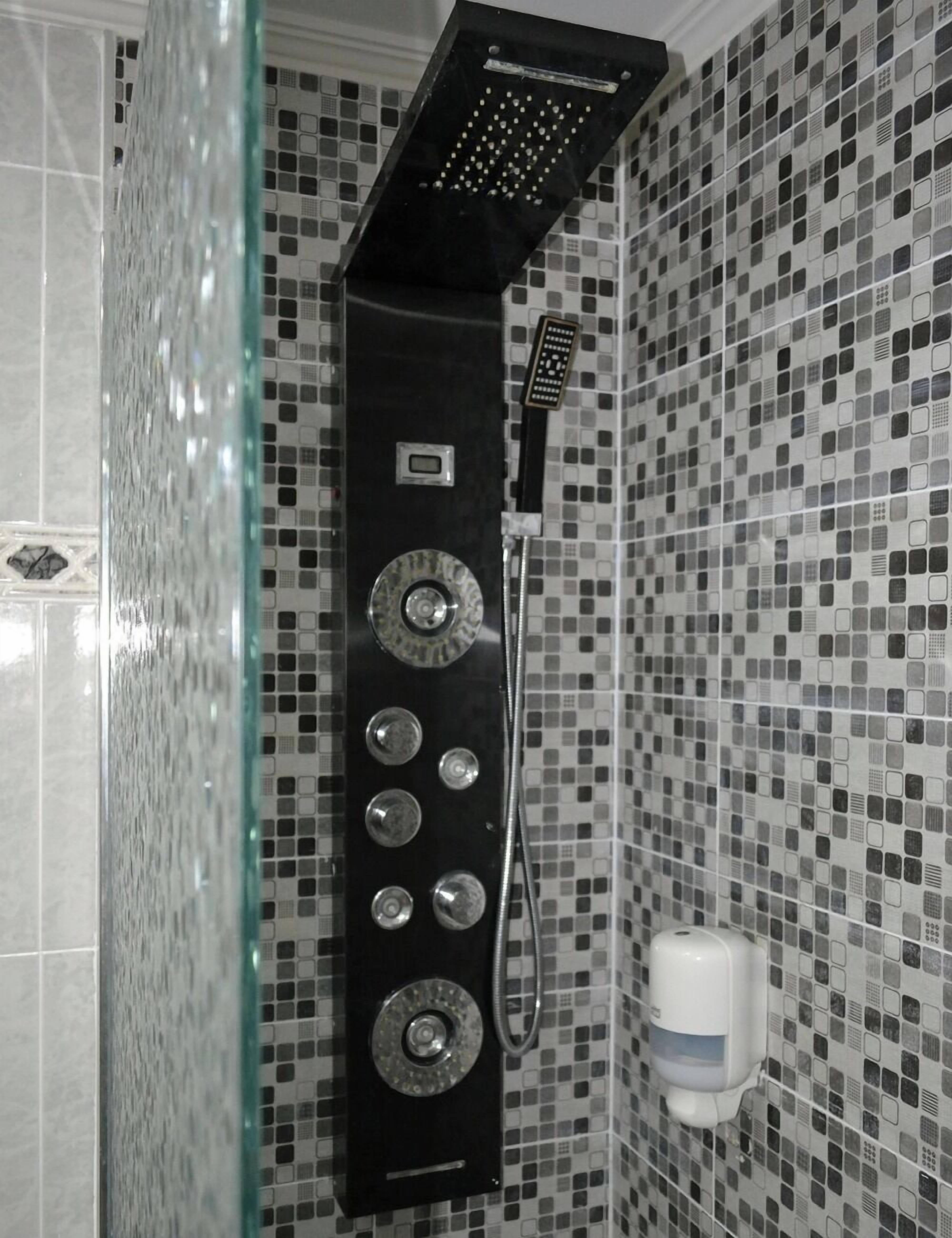 A shower with a control panel, a handheld showerhead, and a soap dispenser on the wall.