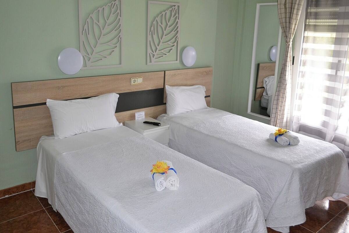 Une chambre d’hôtel avec deux lits, une tête de lit en bois, une table de chevet et un miroir.