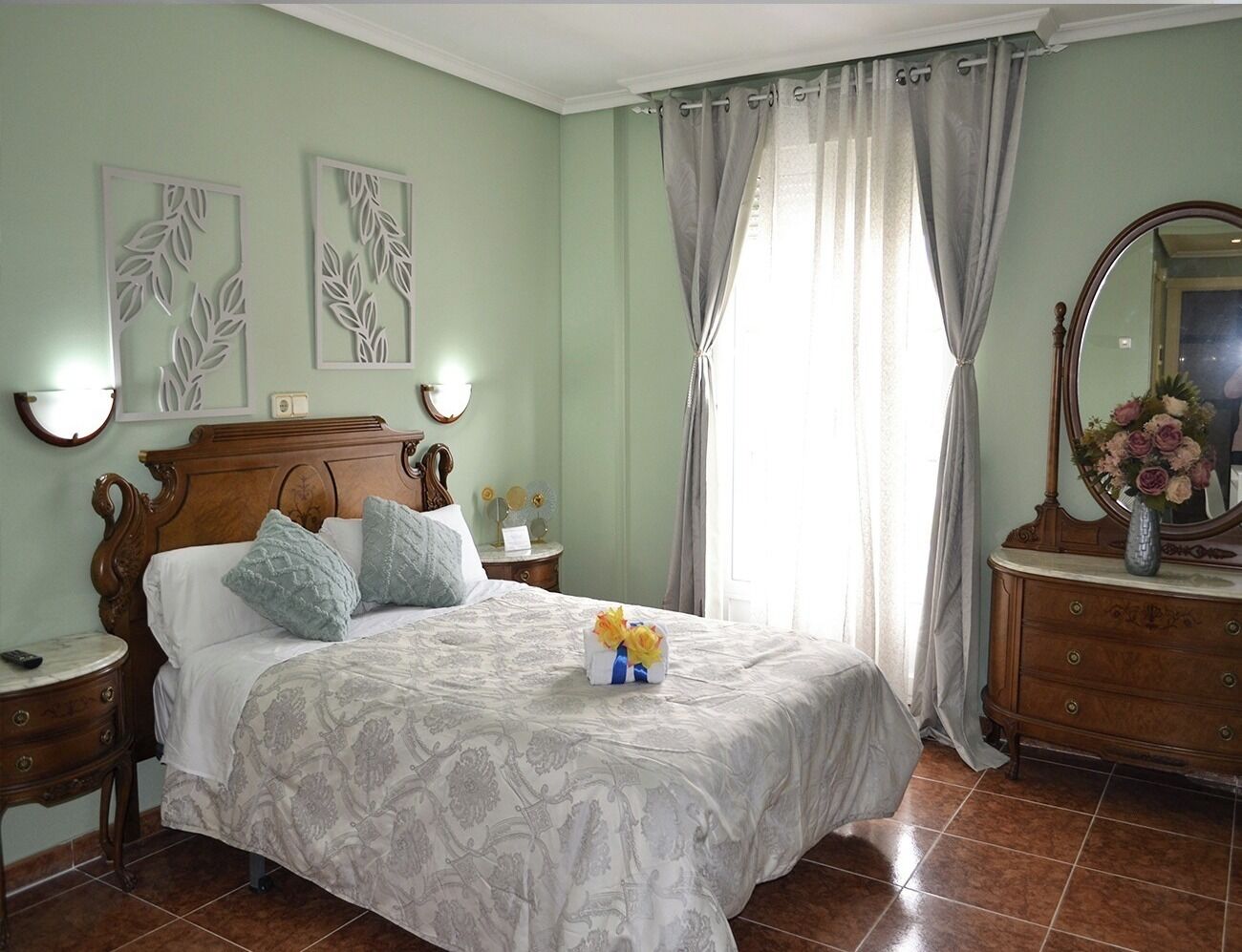 Une chambre à coucher avec un lit en bois, une table de chevet, une commode, un miroir et une fenêtre avec des rideaux.