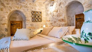 A stone-walled room with a bed, a wooden door, and a wall-mounted light fixture. - Dandy Villas Tower-Built in 17th century (East Mani)