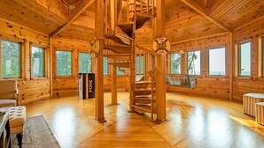 A wooden cabin interior with a spiral staircase, large windows, and a ping pong table.