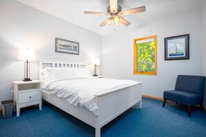 A bedroom with a white bed, two bedside tables, a ceiling fan, and two framed pictures on the wall.