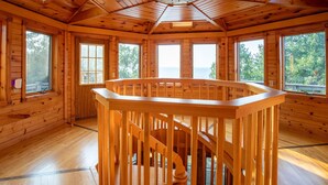 A wooden cabin interior with a central spiral staircase, large windows, and a view of the outdoors.