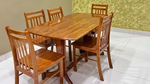 Un espace repas avec une table et des chaises en bois, un mur à texture et un sol carrelé de couleur blanche.