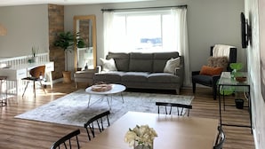 Un salon spacieux avec une grande table à manger en bois, un canapé gris et un ventilateur de plafond.