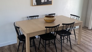 Un coin repas avec une table en bois et des chaises noires, un tableau abstrait en noir et blanc accroché au mur, et un luminaire au plafond.