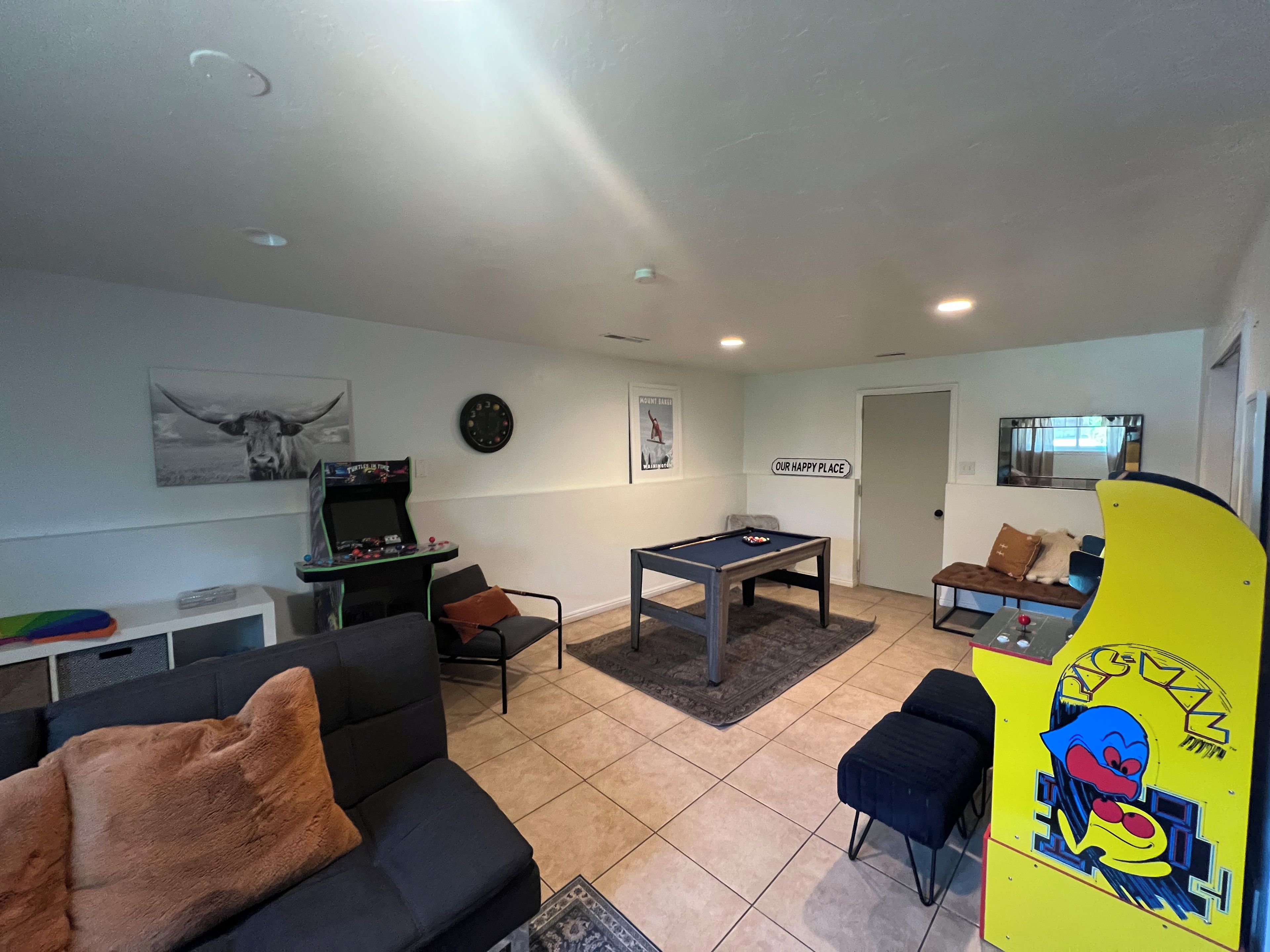 A living room with a pool table, a sofa, a gaming console, and a billiards table.