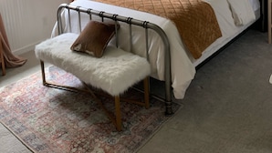 Une chambre à coucher comprenant un lit, une table de chevet, une lampe, un élément de décoration circulaire fixé au mur, une fenêtre avec des rideaux et un petit banc.