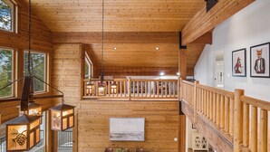 Interior de una cabaña de madera con comedor, escalera de madera y obras de arte en las paredes.