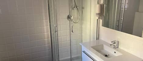 Un baño con ducha de vidrio, lavamanos blanco y bidé.
