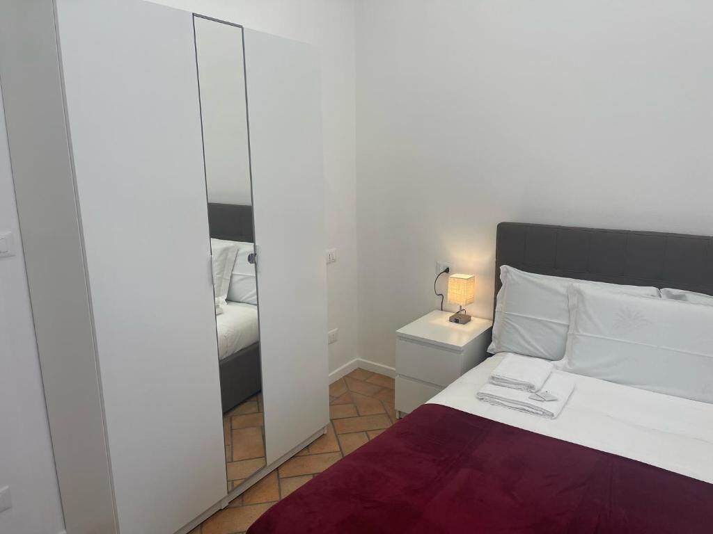 Un dormitorio con una cama, una mesita de noche con lámpara, un armario y un espejo.