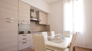 A modern kitchen with a dining table and chairs, built-in appliances, and a large window with curtains.