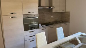 A modern kitchen with light wood cabinets, a stainless steel range hood, and a built-in oven.