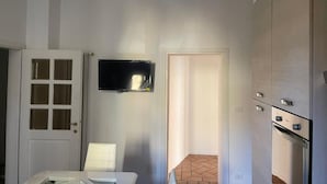 A compact kitchen with a built-in oven, a flat-screen TV, and a door leading to another room.