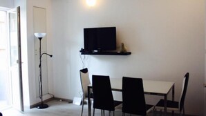 A room with a white wall, a mounted TV, a standing lamp, and a dining table with chairs. - Apartment Central Gardens (București)